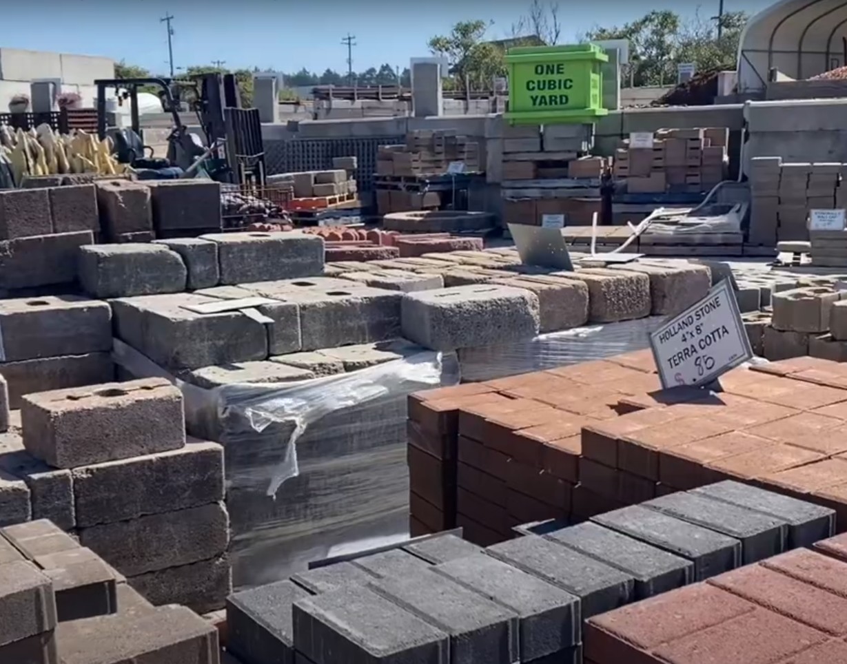 Hardscape material supply yard with organized stacks of pavers, stones, and building materials