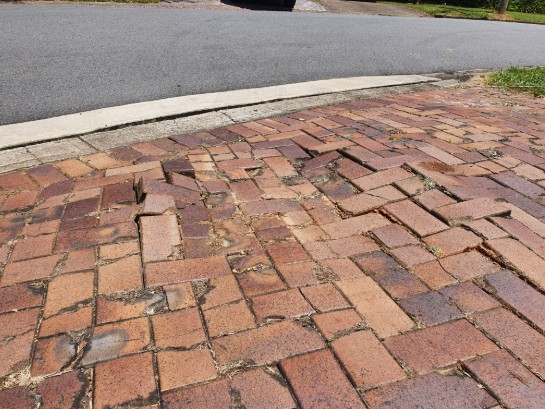 Dangerous driveway with severely damaged and uneven brick pavers creating safety hazards